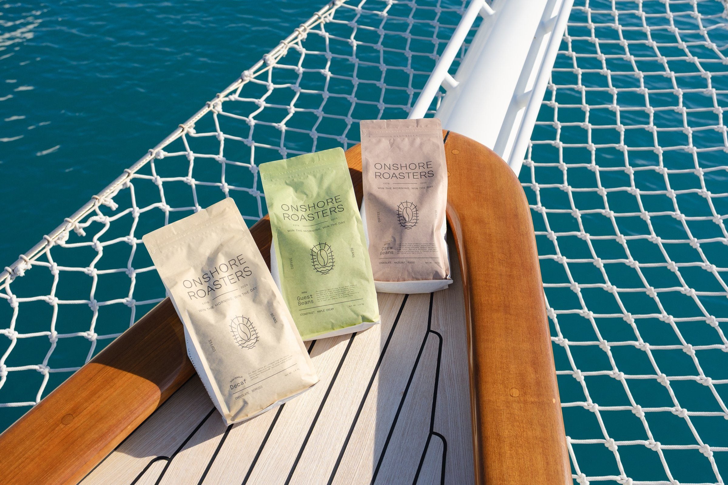 Tres bolsas de café en la proa de teca de un velero clásico, con el mar debajo
