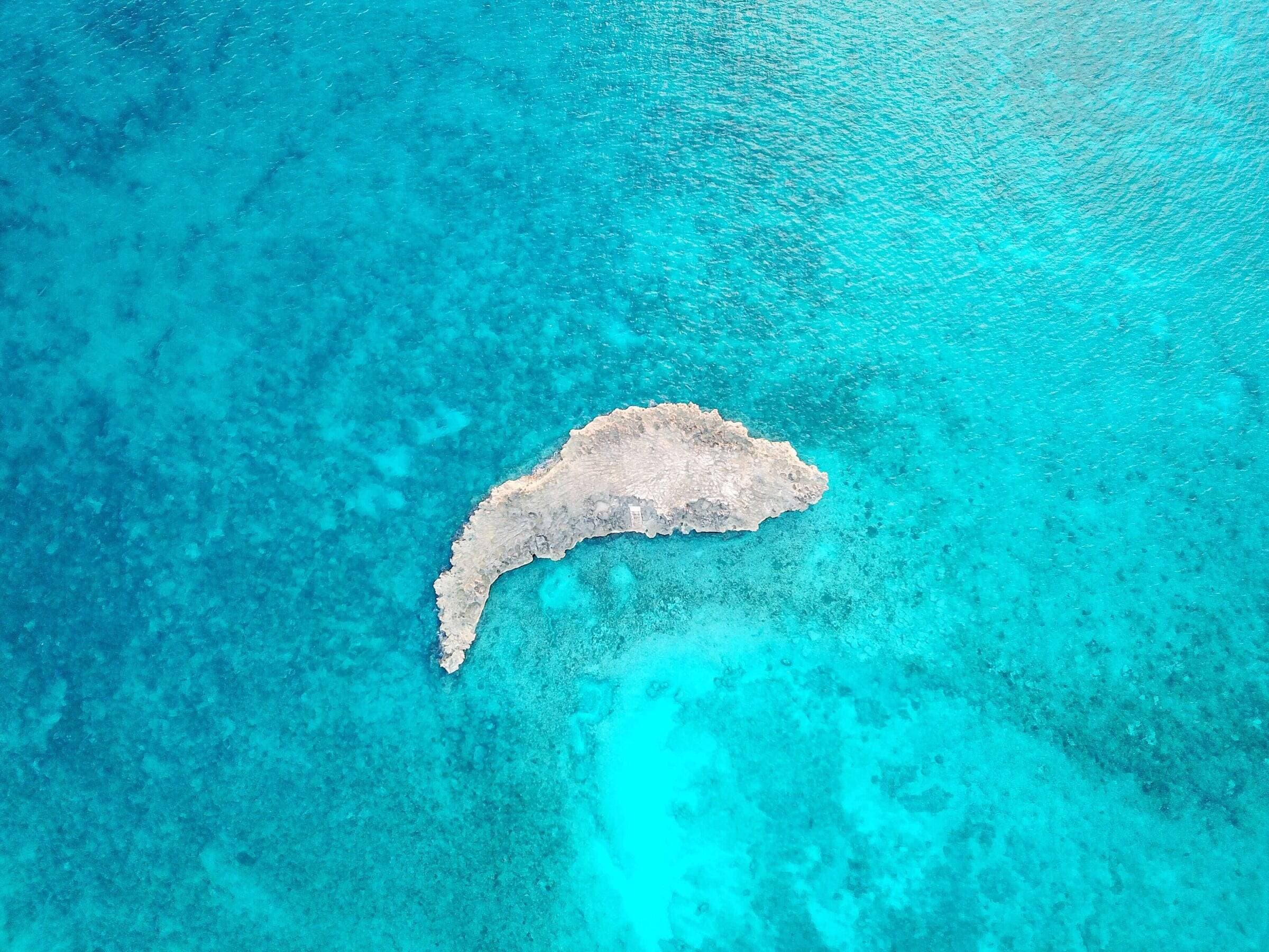 Turquoise shallows around a small rocky island, seen from above