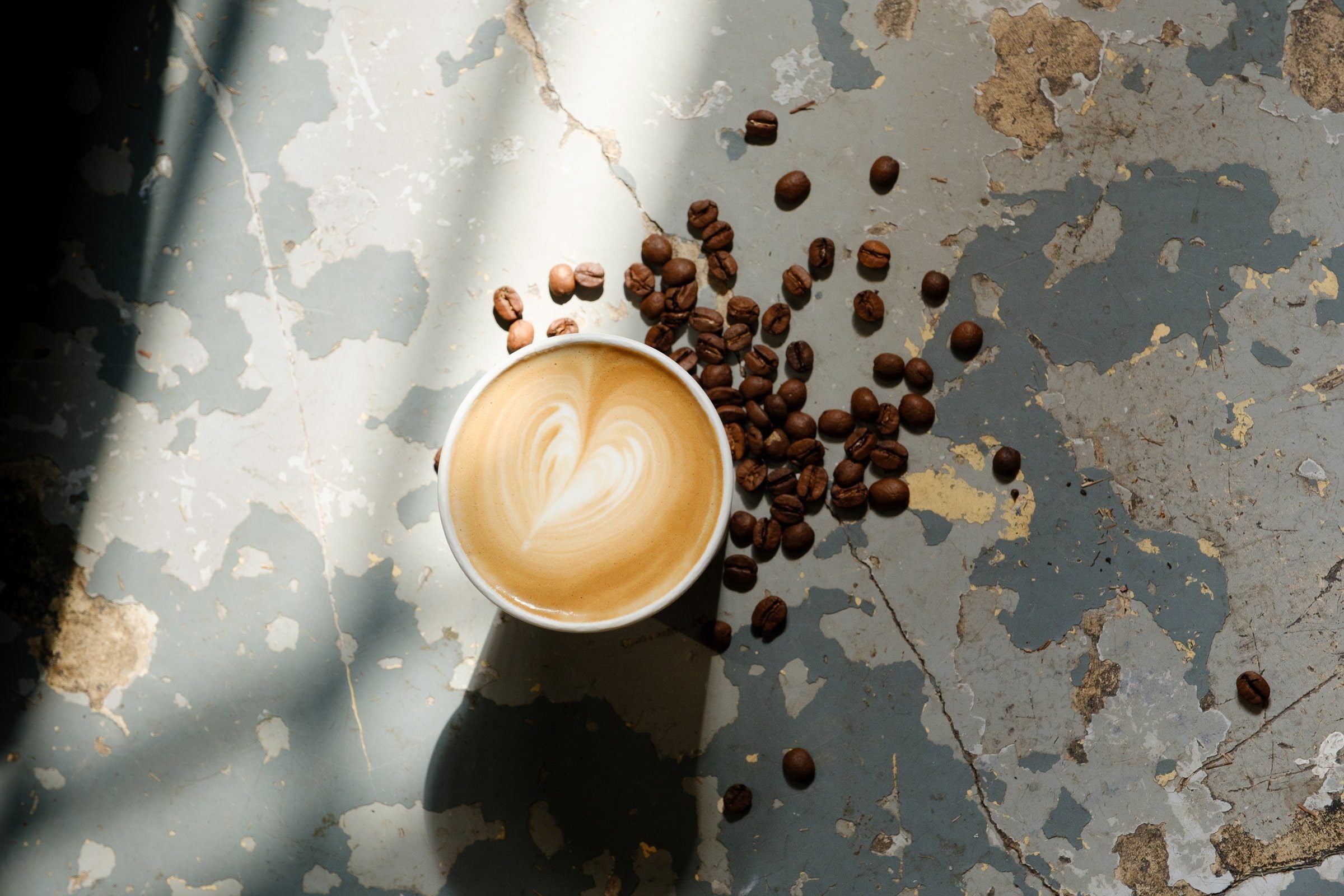 Latte, jossa on sydän, Onshore Roasters -kupissa, ympärillä kahvipapuja