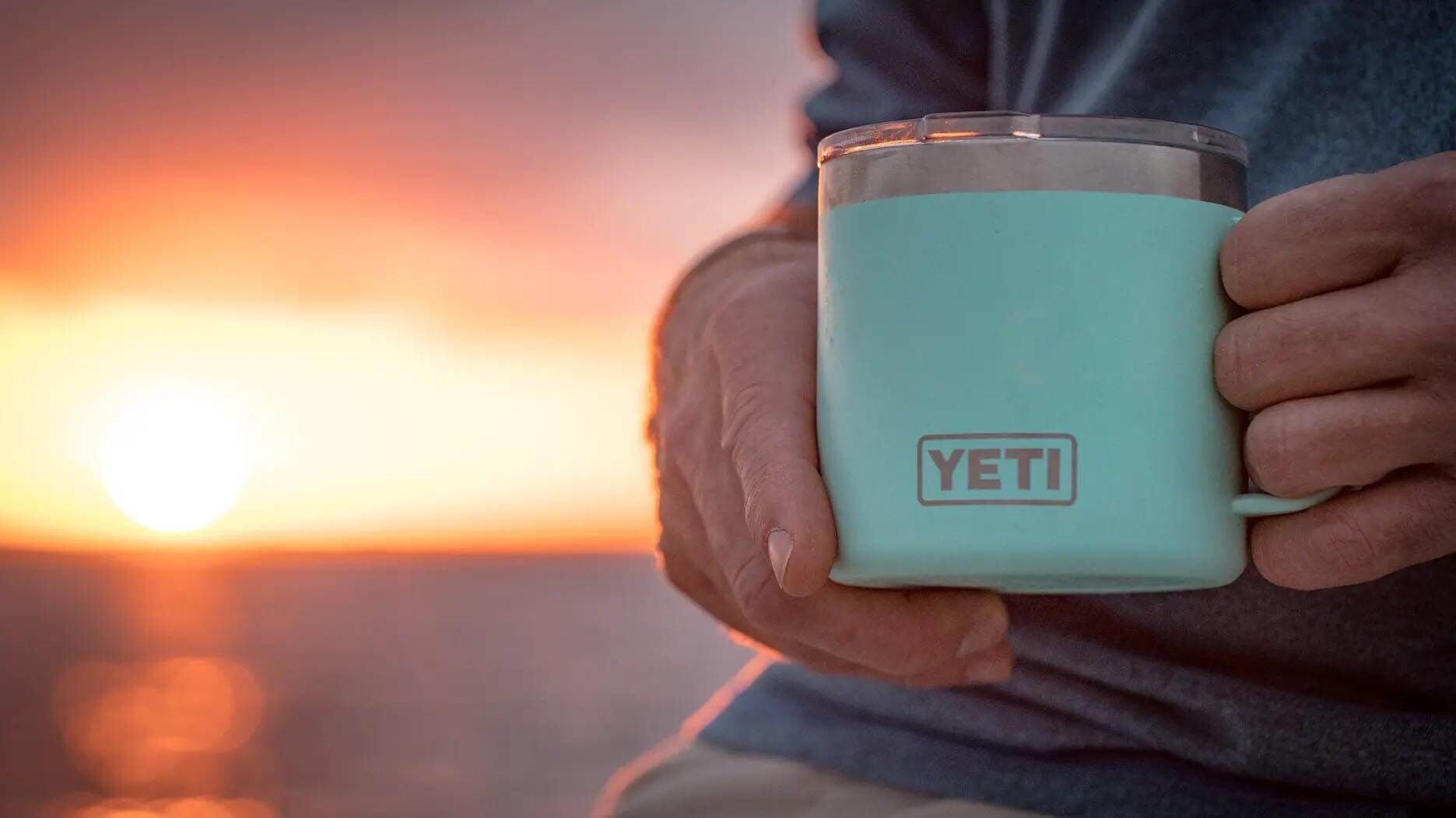 A mug of coffee held up against the sun rising over the sea